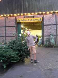 KI generiert: Das Bild zeigt einen beleuchteten Weihnachtsbaum, neben dem eine Person mit einem Lastenfahrrad steht. Das Fahrrad scheint einen weiteren Baum zu transportieren.