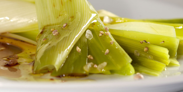 KI generiert: Das Bild zeigt ein Gericht aus gekochten Lauchstücken, die mit grobem Salz und Pfeffer gewürzt sind. Der Lauch liegt auf einem Teller, und es scheint eine Soße darübergegeben zu sein.