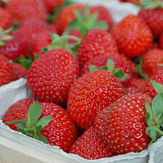 KI generiert: Frische Erdbeeren in einer Pappschale, eng gestapelt mit grünen Blättern.