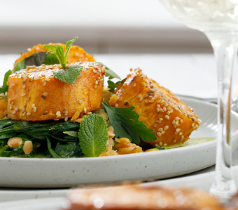 KI generiert: Das Bild zeigt ein Dessert im Glas, das mit einer Löffelportion Croquant und einem Blatt grüne Dekoration versehen ist. Im Hintergrund ist unscharf grüne Dekoration sichtbar.