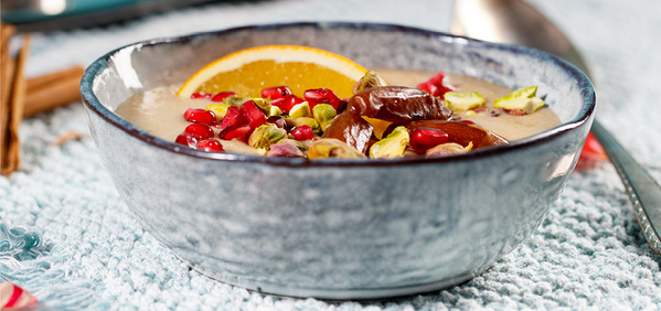 KI generiert: Blaue Schale mit Dessert, garniert mit Pistazien, Granatapfelkernen, Datteln und Orangenscheibe.