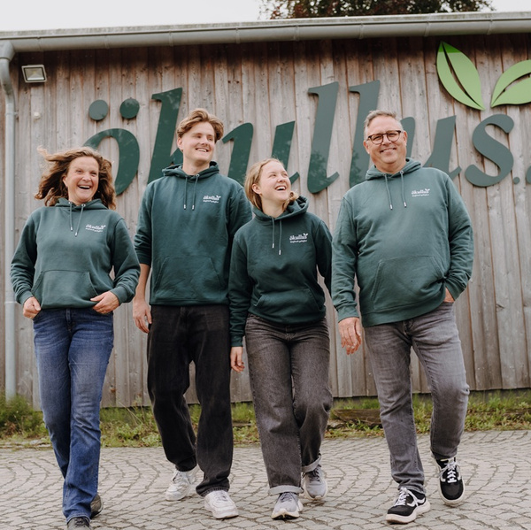 KI generiert: Eine Gruppe von vier Personen in grünen Hoodies steht vor einem Gebäude mit dem Schriftzug "öhlvikus".