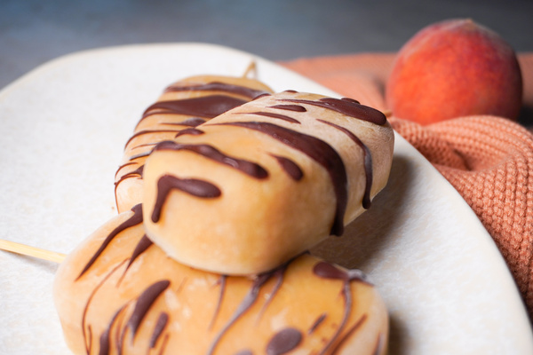 KI generiert: Drei Eis am Stiel mit Schokoladenüberzug auf einem Teller, im Hintergrund ein Pfirsich.