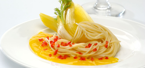 KI generiert: Spaghetti auf gelber Sauce mit fein gehackten roten Paprikastücken und dekorativem Gemüse auf einem Teller.