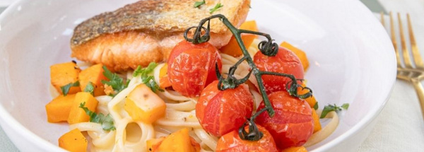 KI generiert: Ein Teller mit gebratenem Lachs, Spaghetti, Kürbisstücken und Rispentomaten.