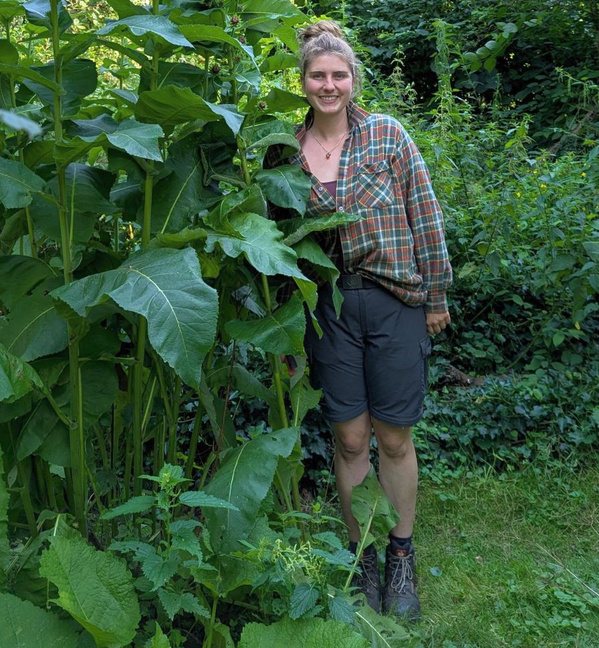 KI generiert: Eine Person steht lächelnd in einem Garten neben großen Pflanzen.
