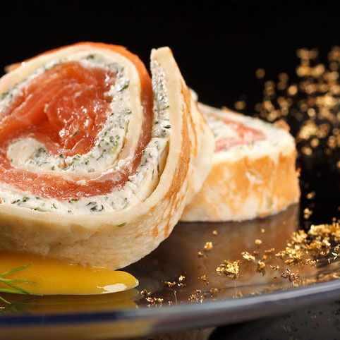 KI generiert: Gerollter Lachs mit Frischkäsefüllung, dekoriert mit goldenen Streuseln auf einem Teller.