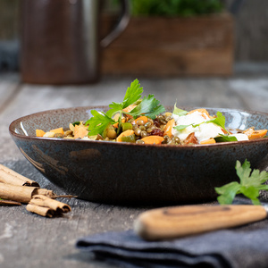 KI generiert: Das Bild zeigt ein Dessert im Glas, das mit einer Löffelportion Croquant und einem Blatt grüne Dekoration versehen ist. Im Hintergrund ist unscharf grüne Dekoration sichtbar.