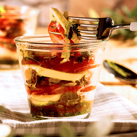 KI generiert: Schichtsalat im Glas mit Tomaten, Mozzarella und Kräutern, dazu eine Gabel.