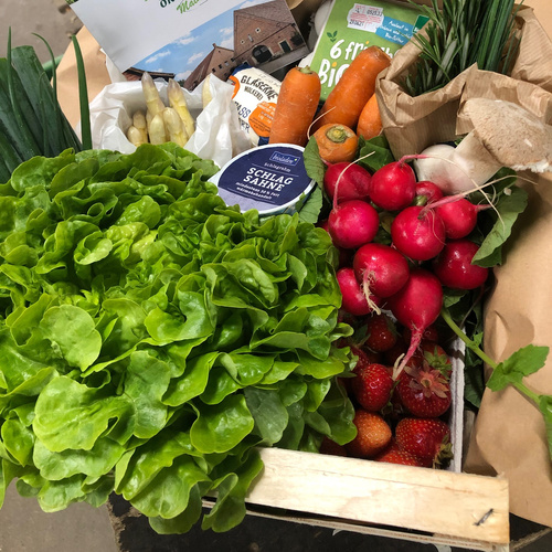 KI generiert: Frische Gemüsekiste mit Salat, Radieschen, Möhren, Spargel, Erdbeeren und Schlagrahm.
