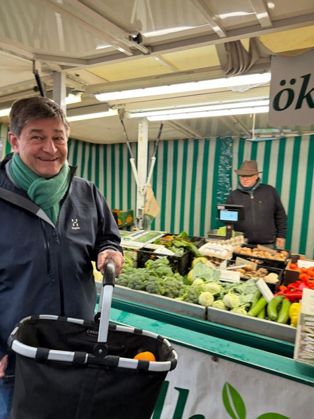 KI generiert: Ein Mann kauft Gemüse an einem Marktstand. Text: "öko".