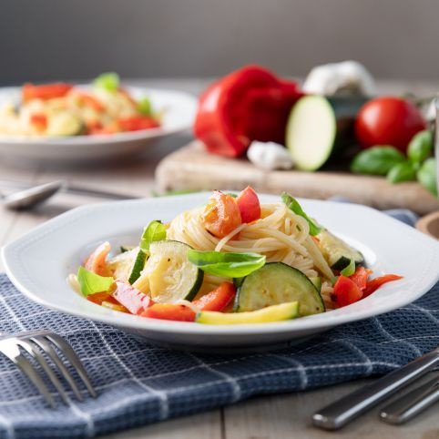 KI generiert: Ein Teller mit Spaghetti und frischem Gemüse auf einem gedeckten Tisch.