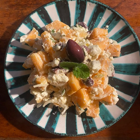 KI generiert: Ein Salat mit Melone, Feta, Oliven und Minze auf einem türkis-farbenen Teller.