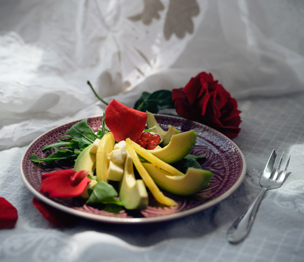 KI generiert: Ein stilvoll angerichteter Salat mit Avocado und roten Blüten auf einem Teller, daneben eine rote Rose.