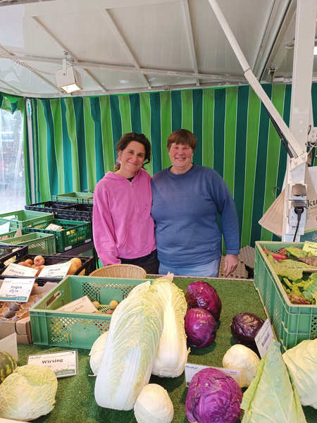 KI generiert: Zwei Personen hinter einem Gemüsestand mit Kohl und Schildern: "Wirsing", "Filderkraut", "Rotkohl".