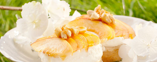 KI generiert: Kleine Kuchen mit Sahne, Pfirsichscheiben und Nüssen auf einem Teller, dekoriert mit weißen Blüten.