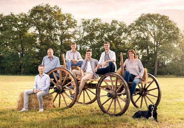 KI generiert: Eine Gruppe von Menschen und ein Hund posieren auf einem Heuwagen in einer ländlichen Umgebung.