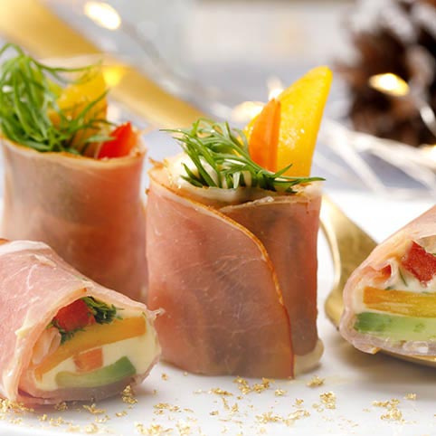 KI generiert: Vorspeisen mit Schinken, Frischkäse, Gemüse und Kräutern, dekorativ angerichtet auf einem Teller.
