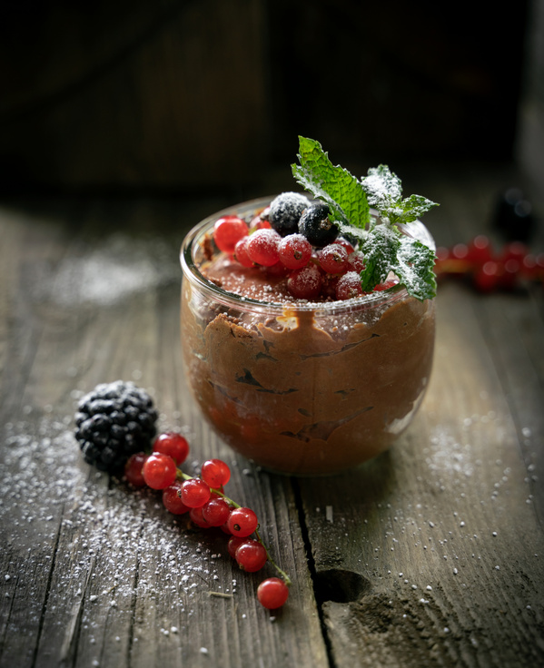 KI generiert: Ein Glas Dessert mit Schokoladenmousse, Beeren und Minzblättern, dekoriert mit Puderzucker.