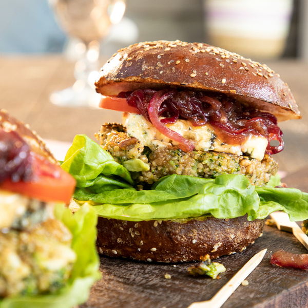 KI generiert: Ein Burger mit Gemüsepatty, Salat, Tomate und karamellisierten Zwiebeln auf einem dunklen Sesam-Brötchen.