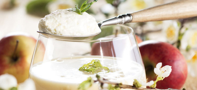 KI generiert: Das Bild zeigt ein Dessert im Glas, das mit einer Löffelportion Croquant und einem Blatt grüne Dekoration versehen ist. Im Hintergrund ist unscharf grüne Dekoration sichtbar.