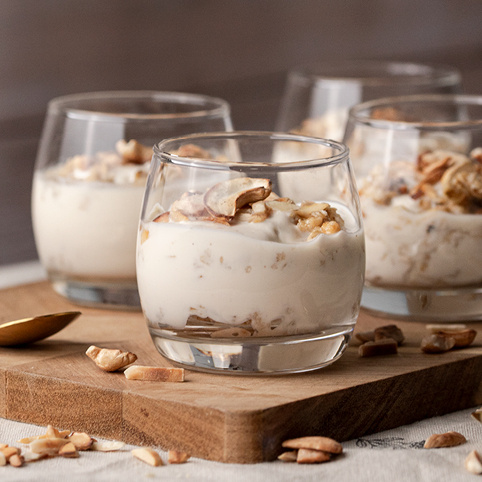 KI generiert: Gläser mit cremigem Dessert und Nüssen auf einem Holzbrett.