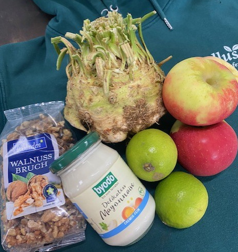 KI generiert: Gemüse, Äpfel, Limetten, ein Glas Mayonnaise und Walnussbruch liegen zusammen. Text: "WALNUSS BRUCH", "byodo".