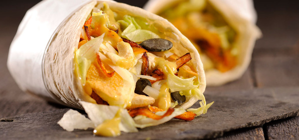 KI generiert: Das Bild zeigt einen gefüllten Wrap, der mit frischem Gemüse und Saucen versehen ist. Der Fokus liegt auf der appetitlichen Nahaufnahme des gefüllten Wraps auf einem dunklen Untergrund.