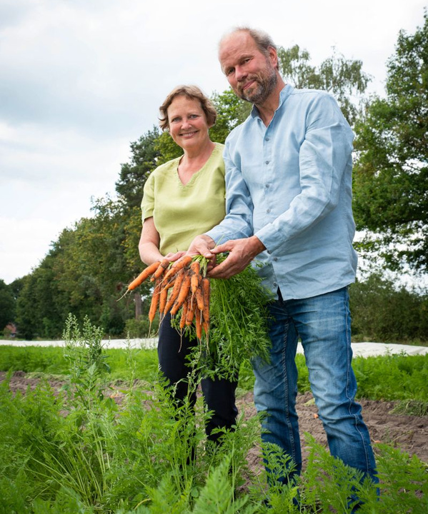KI generiert: Zwei Personen stehen in einem Feld und halten einen Bund Karotten in den Händen.