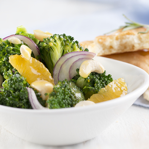 KI generiert: Ein frischer Brokkoli-Salat mit Orangen, roten Zwiebeln und Mandeln in einer weißen Schüssel.