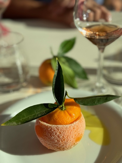 KI generiert: Das Bild zeigt eine kunstvoll angerichtete Orange mit Blättern auf einem Teller, daneben steht ein Glas mit roséfarbenem Getränk. Es handelt sich offensichtlich um ein sorgfältig präsentiertes Gericht oder Dekoration.