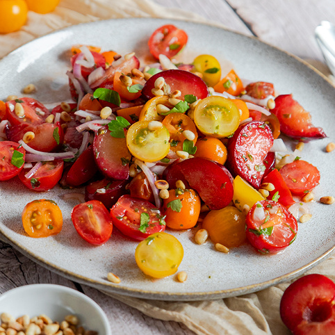 KI generiert: Ein bunter Tomatensalat mit verschiedenen Tomaten, Pflaumen, Pinienkernen und Kräutern auf einem Teller.