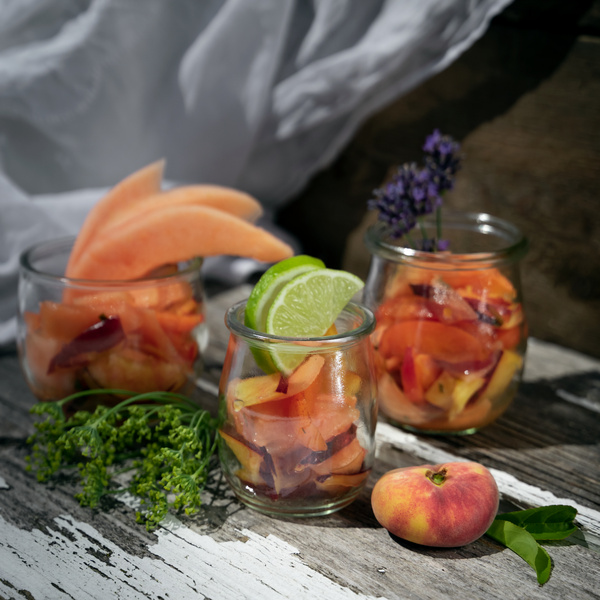 KI generiert: Drei Gläser mit frischen Obstsalaten, garniert mit Limette, Melone und Lavendel auf Holzuntergrund.