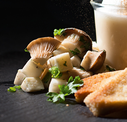KI generiert: Das Bild zeigt ein elegantes Essen mit panierten Pilzen, gekochten Pilzen und einer Art Soße oder Suppe in einem Glas. Die Präsentation auf einer dunklen Platte lässt ein anspruchsvolles Gericht vermuten.
