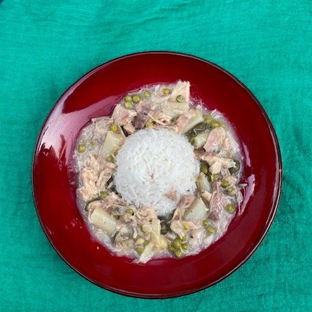 KI generiert: Ein Teller Reis mit Thunfisch, Erbsen und Soße auf grünem Hintergrund.