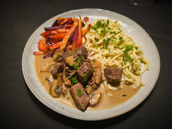 KI generiert: Ein Teller mit Pasta, Fleisch in Pilzsauce und glasiertem Gemüse.