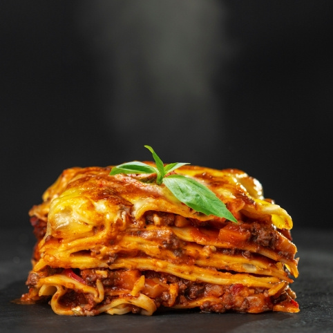 KI generiert: Ein Stück Lasagne mit einer Basilikum-Dekoration und aufsteigendem Dampf.