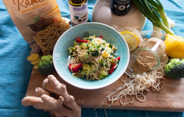 KI generiert: Ein Teller Nudelsalat mit frischem Gemüse und Zutaten. Text: "Ramen Brown Rice Noodles", "Erdnussöl".