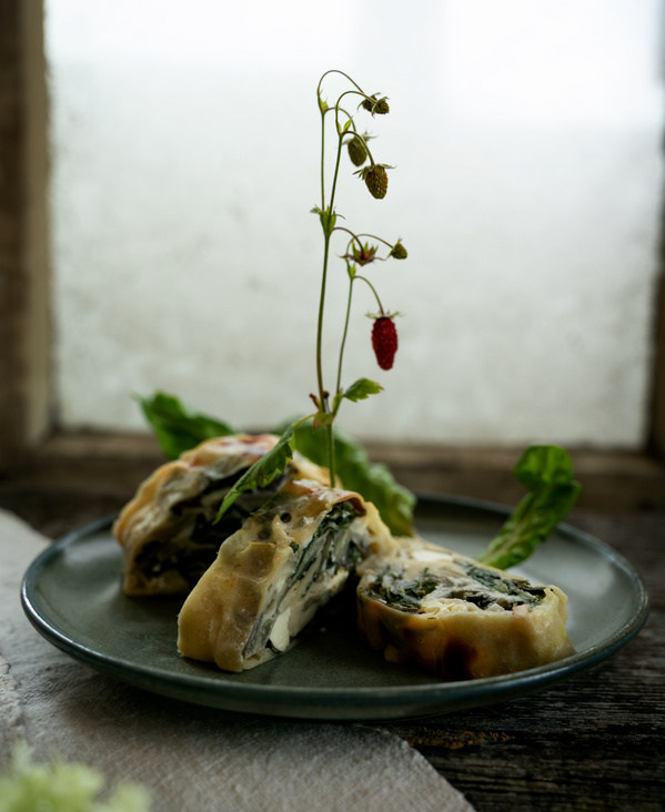 KI generiert: Gebackener Gemüsestrudel auf einem Teller, dekoriert mit einem Zweig wilder Erdbeeren.