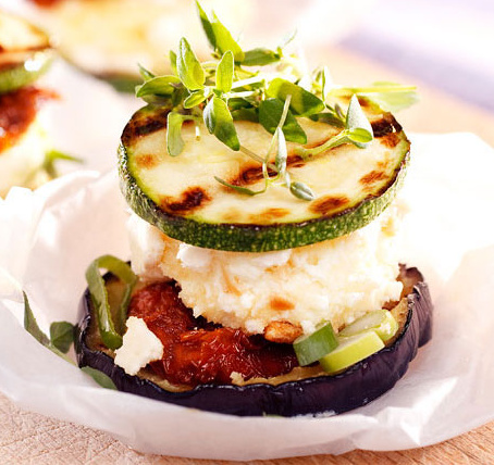 KI generiert: Ein Gourmet-Gemüseturm aus Aubergine, Zucchini, Frischkäse und frischen Kräutern auf Pergamentpapier.