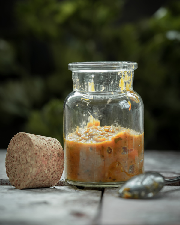 KI generiert: Das Bild zeigt ein Glas mit einem Korkverschluss, das eine pastenartige Mischung enthält, auf einem Tisch. Im Vordergrund liegt ein Löffel neben dem Glas.