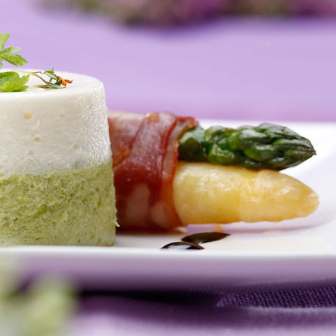 KI generiert: Ein dekorativ angerichteter Teller mit Panna cotta und Spargel im Speckmantel.