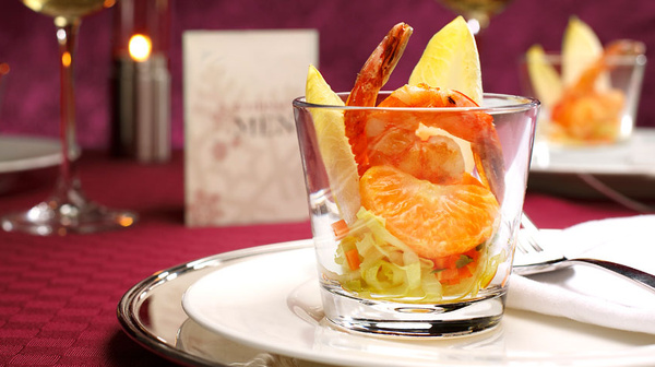 KI generiert: Ein elegantes Glas mit Garnelen und Mandarine, stilvoll angerichtet auf einem Teller.