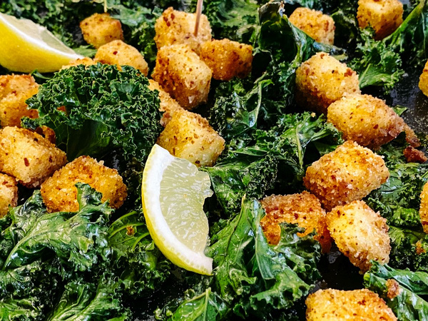 KI generiert: Das Bild zeigt gebratene Tofu-Würfel mit knusprigem Grünkohl und Zitronenspalten. Der Fokus liegt auf dem appetitlichen Kontrast zwischen den goldbraunen Tofuwürfeln und dem grünen Gemüse.