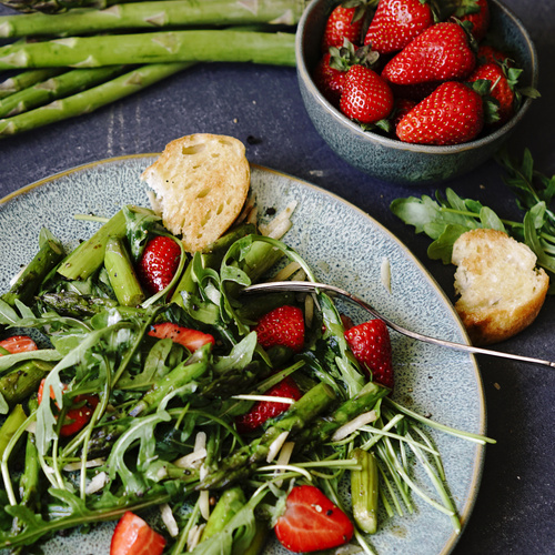 KI generiert: Ein frischer Salat mit grünem Spargel, Erdbeeren und Rucola auf einem Teller.