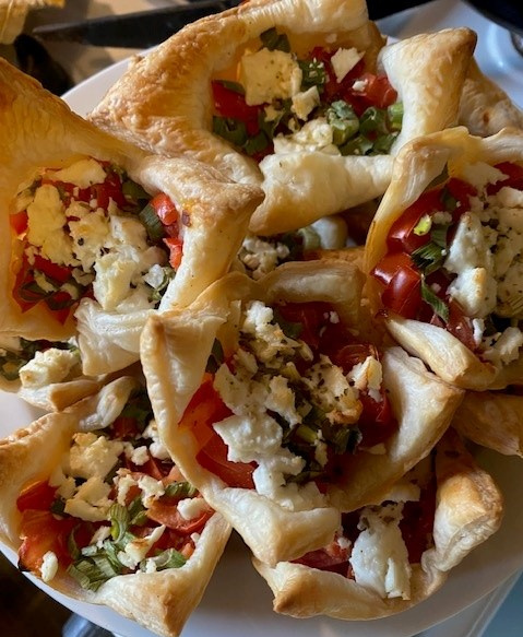 KI generiert: Herzhafte Blätterteigtaschen mit Feta, Tomaten und Frühlingszwiebeln auf einem Teller.