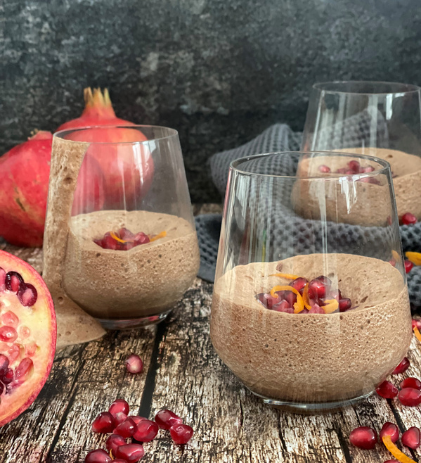 KI generiert: Schokoladenmousse in Gläsern, garniert mit Granatapfelkernen und Orangenzeste. Granatapfel im Hintergrund.