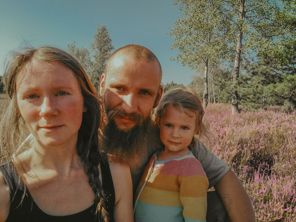KI generiert: Auf dem Bild sind drei Personen zu sehen, die in einer Landschaft mit blühender Heide stehen. Im Hintergrund sind Bäume und ein klarer, blauer Himmel erkennbar.