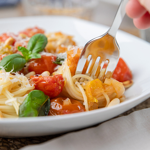 KI generiert: Spaghetti mit Tomaten, Basilikum und Parmesan auf einer weißen Platte, Gabel sticht in die Nudeln.