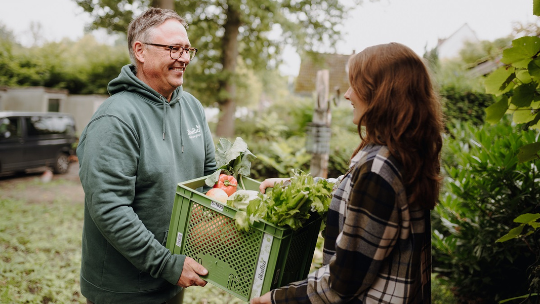 KI generiert: Ein Mann und eine Frau übergeben sich eine Gemüsekiste im Freien.
